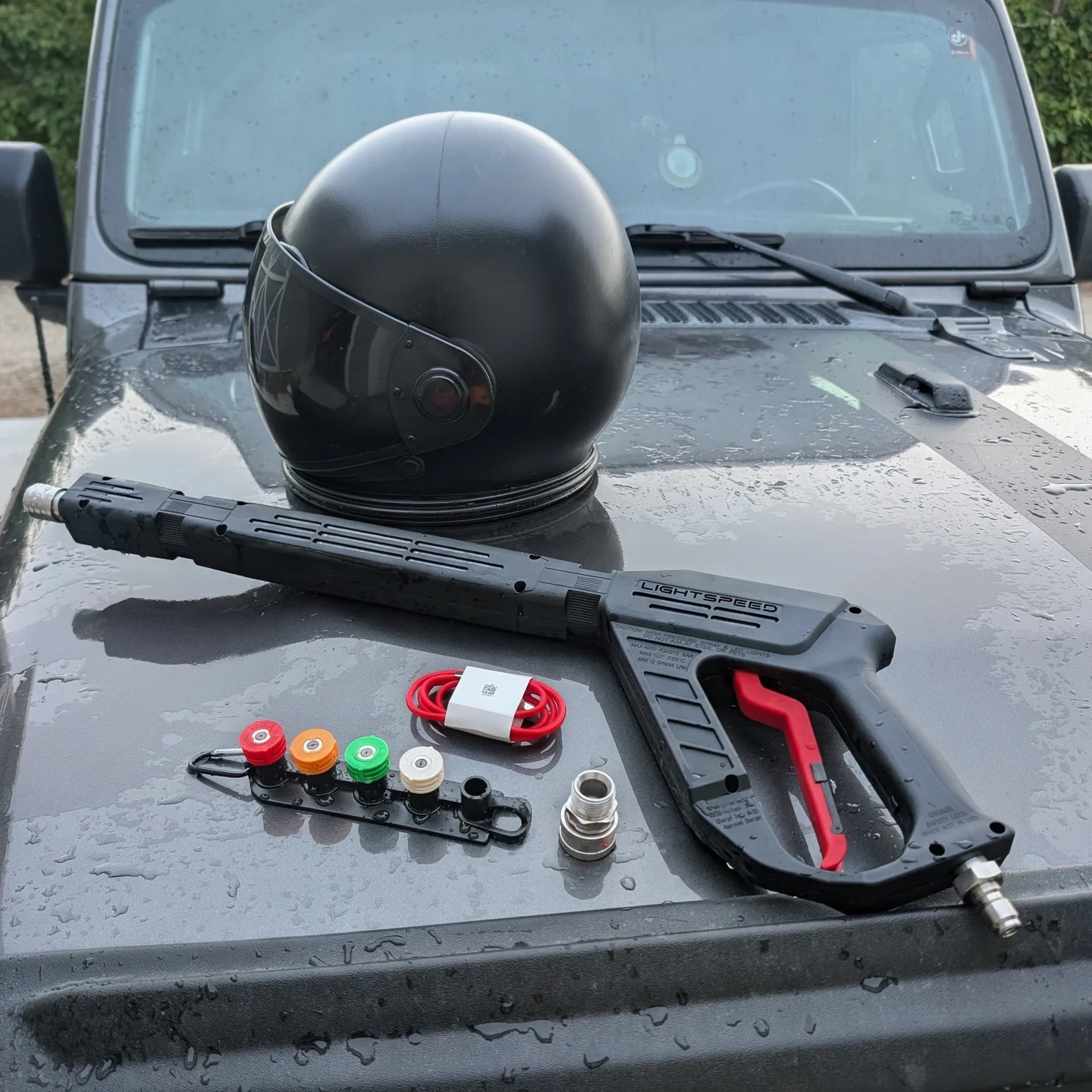 Lightspeed Blaster, black helmet, four nozzles, adapter and charging cable on a wet truck hood