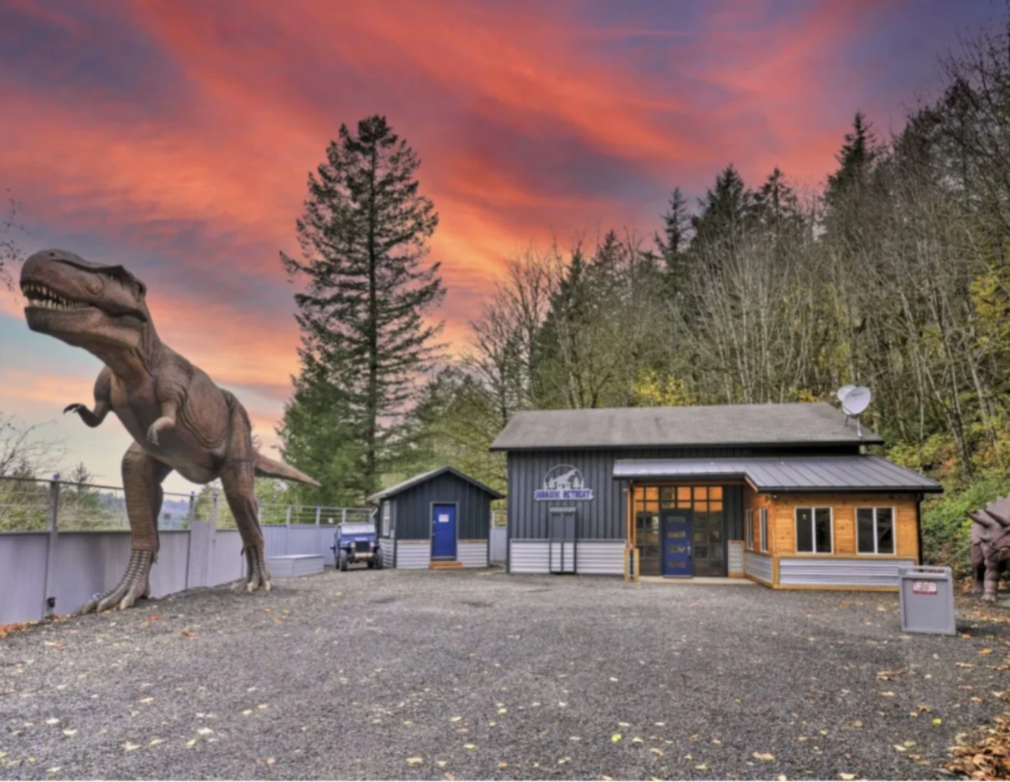 Jurassic Retreat vacation rental with a giant T-Rex outside beneath a pink evening sky