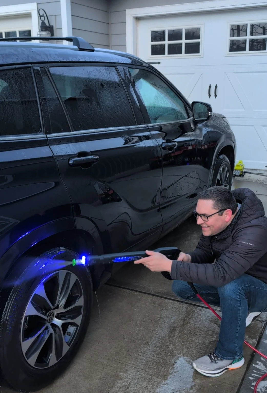 Todd Perkins squatting beside a car and testing an early Lightspeed Blaster with blue illuminated water